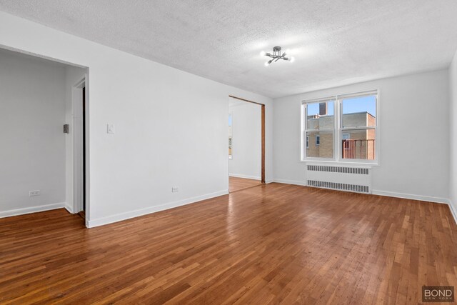 spare room featuring radiator heating unit, wood finished floors, baseboards, and a textured ceiling