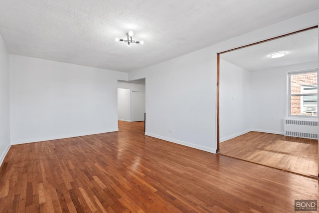 unfurnished room featuring baseboards, a textured ceiling, radiator heating unit, and hardwood / wood-style flooring