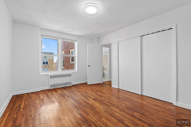 unfurnished bedroom featuring radiator, a closet, baseboards, and wood-type flooring