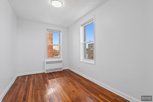 unfurnished room featuring a textured ceiling, baseboards, dark wood finished floors, and radiator