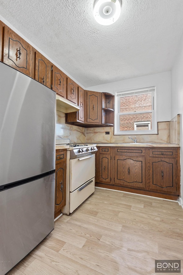kitchen with a textured ceiling, white gas range, light countertops, freestanding refrigerator, and light wood-type flooring