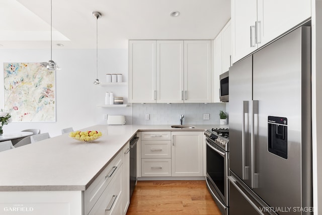 kitchen with stainless steel appliances, a peninsula, white cabinetry, and decorative light fixtures