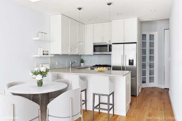 kitchen featuring appliances with stainless steel finishes, a peninsula, hanging light fixtures, light countertops, and white cabinetry