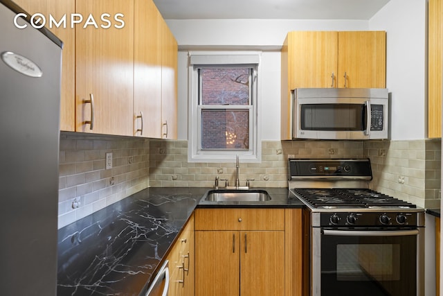 kitchen with stainless steel appliances, a sink, decorative backsplash, dark stone counters, and brown cabinetry