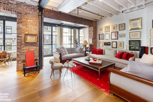 living area featuring beam ceiling, brick wall, track lighting, and hardwood / wood-style flooring