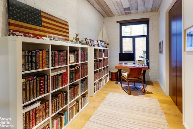 office with wood ceiling, brick wall, bookshelves, and wood finished floors