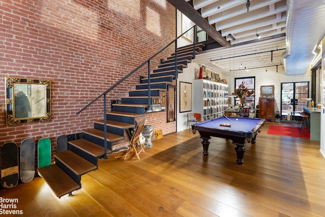 recreation room with a towering ceiling, wood-type flooring, brick wall, and pool table