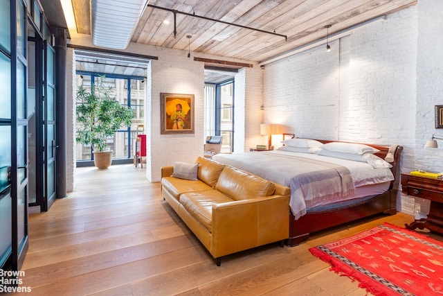 bedroom with brick wall, wooden ceiling, light wood-style flooring, and access to exterior