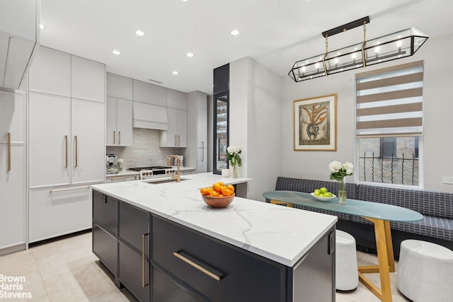 kitchen with breakfast area, gray cabinets, backsplash, a sink, and light stone countertops