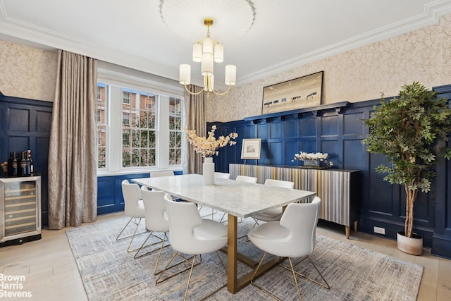 dining room featuring a chandelier, wine cooler, wainscoting, wallpapered walls, and crown molding