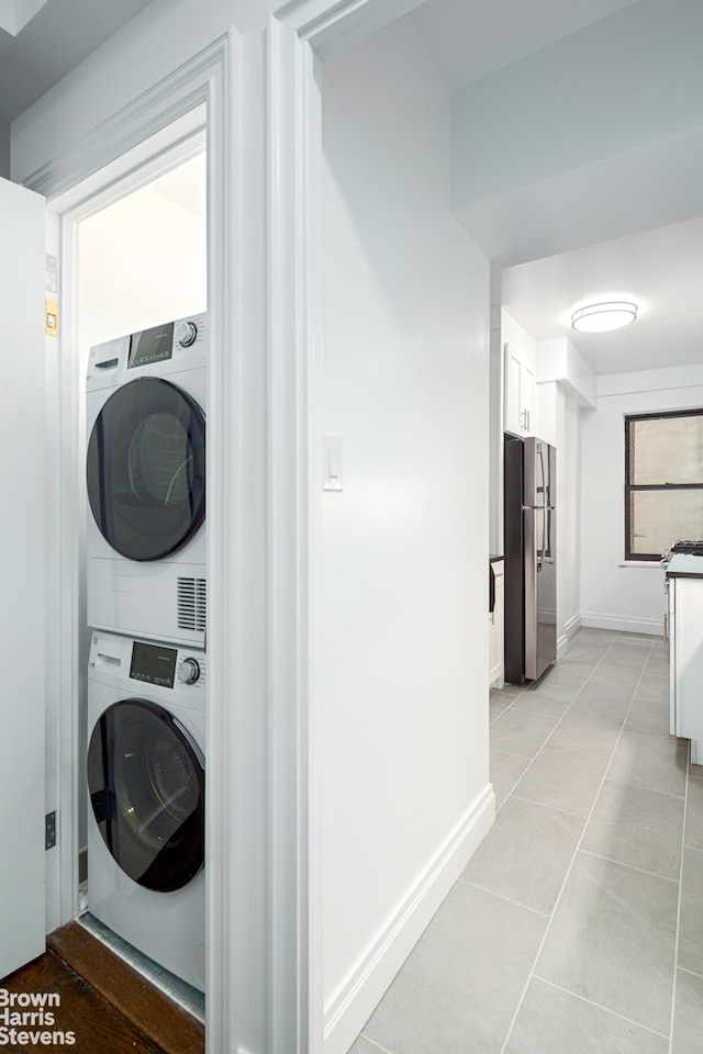 washroom featuring laundry area, stacked washer / dryer, light tile patterned flooring, and baseboards