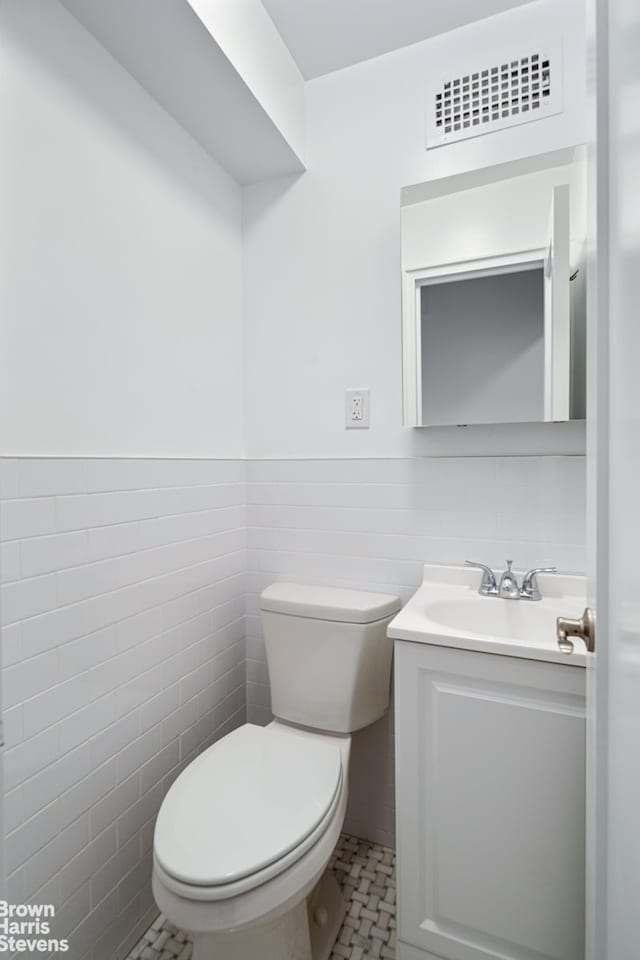 half bathroom with visible vents, toilet, a wainscoted wall, vanity, and tile walls