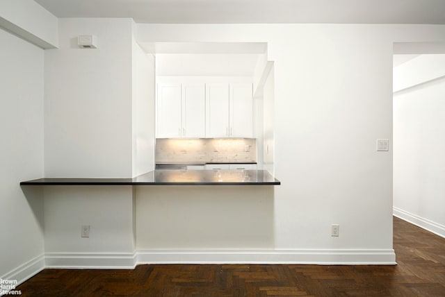 kitchen with baseboards, tasteful backsplash, dark countertops, and white cabinets