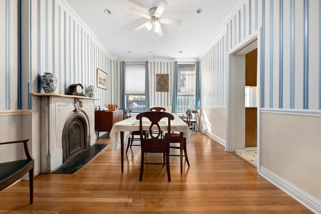 dining area featuring a fireplace with flush hearth, wood finished floors, a ceiling fan, baseboards, and crown molding