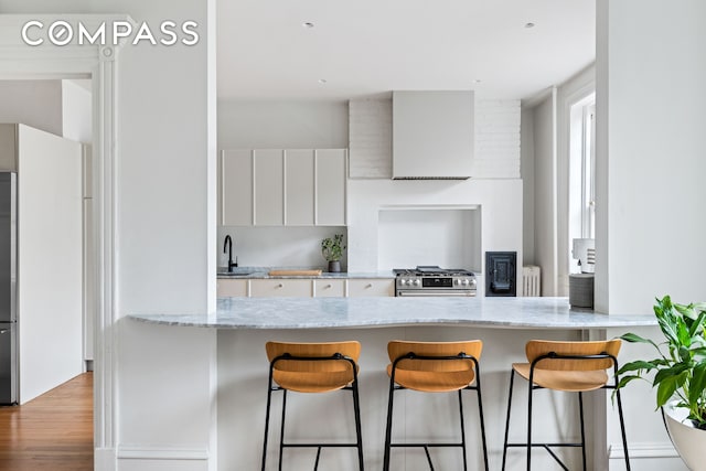 kitchen with a breakfast bar, a sink, white cabinetry, radiator, and stainless steel range with gas cooktop