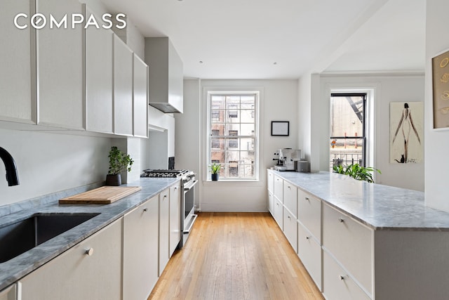 kitchen featuring light wood-style flooring, light stone counters, a sink, a peninsula, and gas range