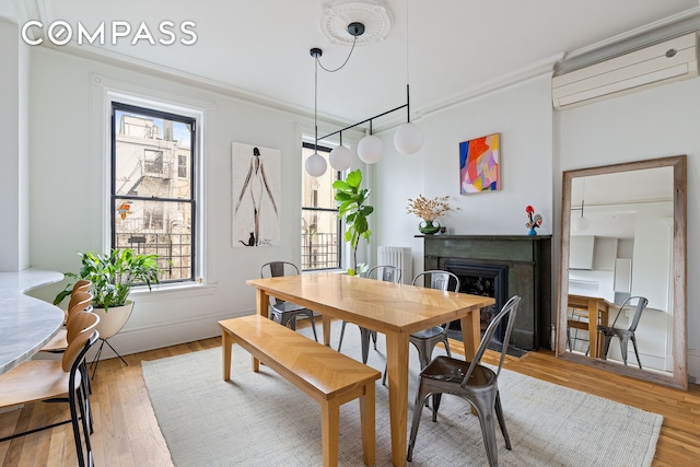 dining space with a fireplace, a wall mounted AC, light wood-style floors, and crown molding