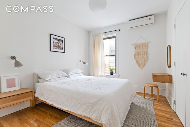 bedroom with light wood finished floors, baseboards, and a wall unit AC