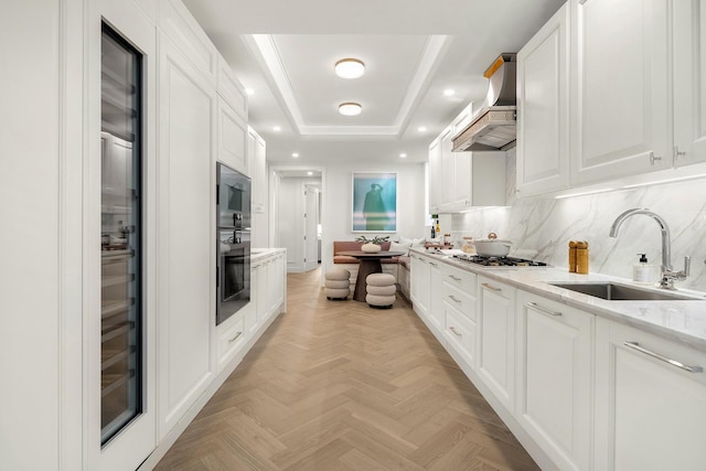 kitchen featuring a sink, white cabinetry, wall chimney exhaust hood, tasteful backsplash, and a raised ceiling