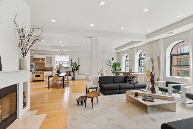 living area featuring light wood-type flooring, visible vents, recessed lighting, a fireplace, and a raised ceiling