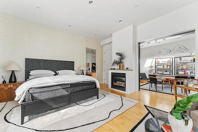 bedroom featuring a glass covered fireplace and light wood-style flooring