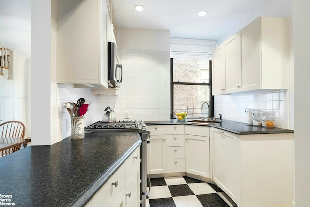 kitchen featuring white cabinets, dark countertops, stainless steel appliances, light floors, and a sink