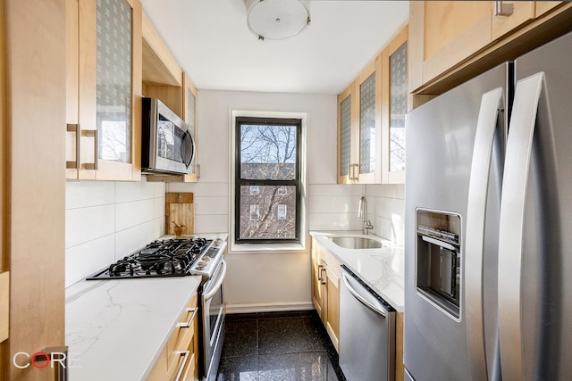 kitchen with granite finish floor, a sink, appliances with stainless steel finishes, light stone countertops, and glass insert cabinets