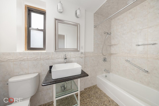 bathroom featuring toilet, a wainscoted wall, a sink, tile walls, and shower / washtub combination