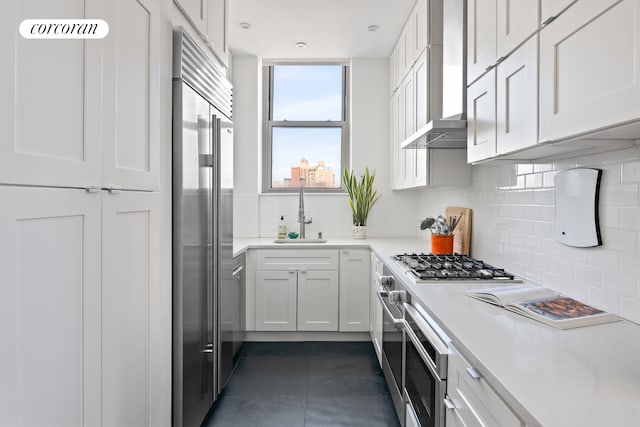 kitchen with stainless steel appliances, a sink, light countertops, decorative backsplash, and wall chimney exhaust hood