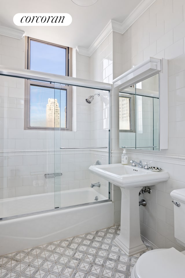 bathroom with toilet, tile walls, combined bath / shower with glass door, and crown molding