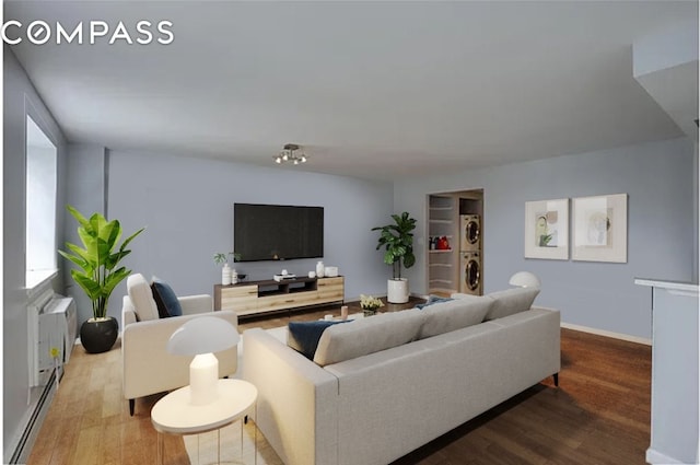 living room with a baseboard heating unit, stacked washer / drying machine, baseboards, and wood finished floors