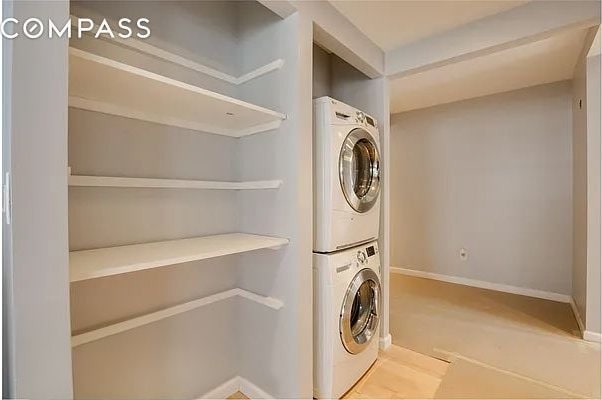 clothes washing area featuring stacked washer and dryer, laundry area, and baseboards