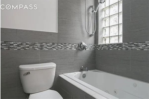 bathroom featuring a combined bath / shower with jetted tub, toilet, and tile walls