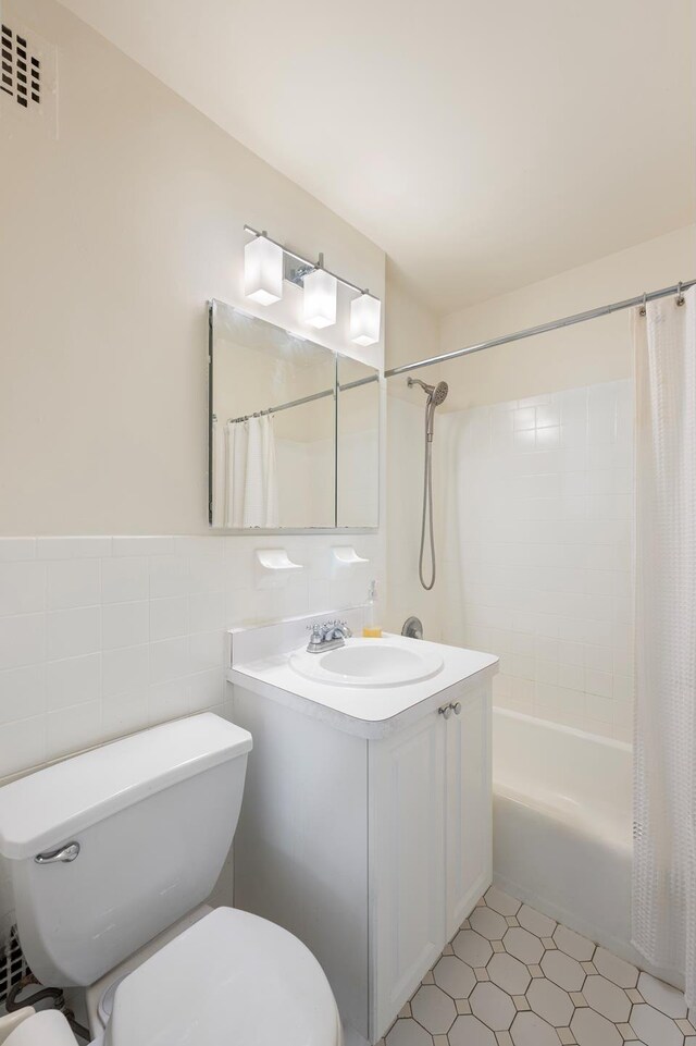 bathroom with toilet, a wainscoted wall, vanity, tile walls, and shower / bath combo