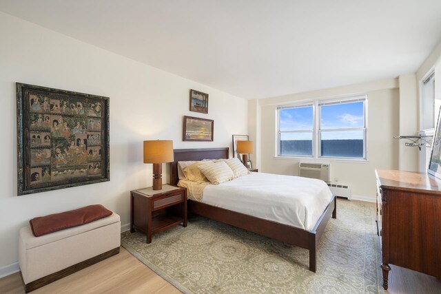 bedroom featuring a baseboard heating unit, a wall unit AC, light wood-style flooring, and baseboards