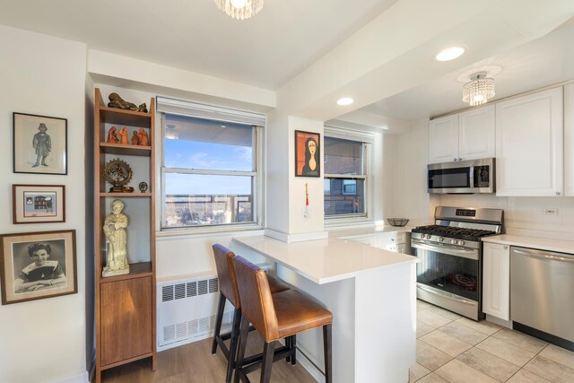 kitchen with stainless steel appliances, light countertops, radiator heating unit, white cabinetry, and a peninsula