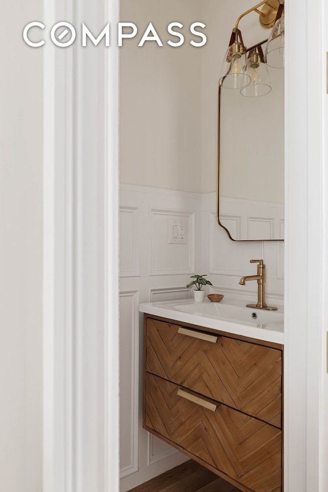 bathroom featuring a wainscoted wall, a decorative wall, and vanity