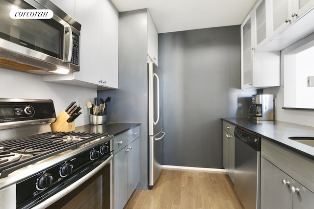 kitchen with glass insert cabinets, dark countertops, white cabinets, and appliances with stainless steel finishes