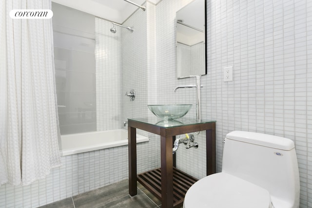 bathroom featuring tile walls, toilet, tiled shower / bath combo, a sink, and tile patterned flooring