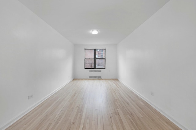 empty room featuring baseboards, light wood finished floors, and radiator heating unit