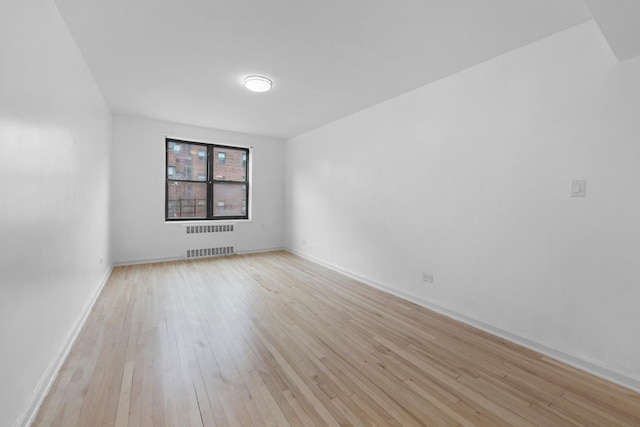 spare room with radiator, light wood-style flooring, and baseboards