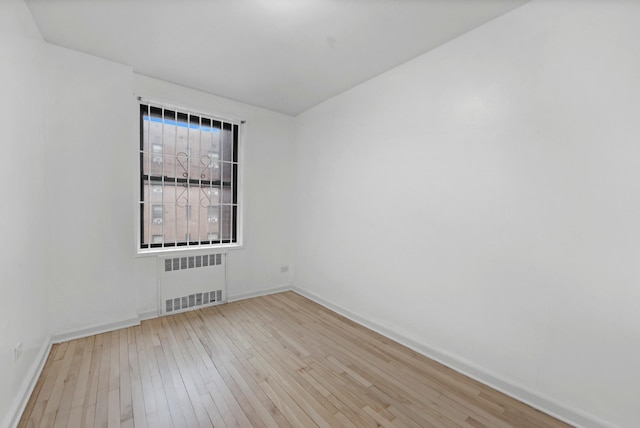 empty room with light wood-type flooring, radiator heating unit, and baseboards