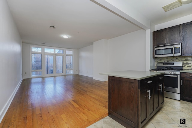 kitchen with visible vents, a kitchen island, baseboards, appliances with stainless steel finishes, and backsplash