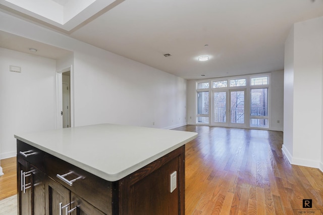 kitchen featuring dark brown cabinetry, baseboards, open floor plan, light countertops, and light wood-style flooring