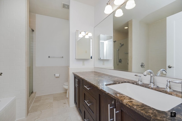 bathroom featuring visible vents, tile walls, a stall shower, vanity, and toilet