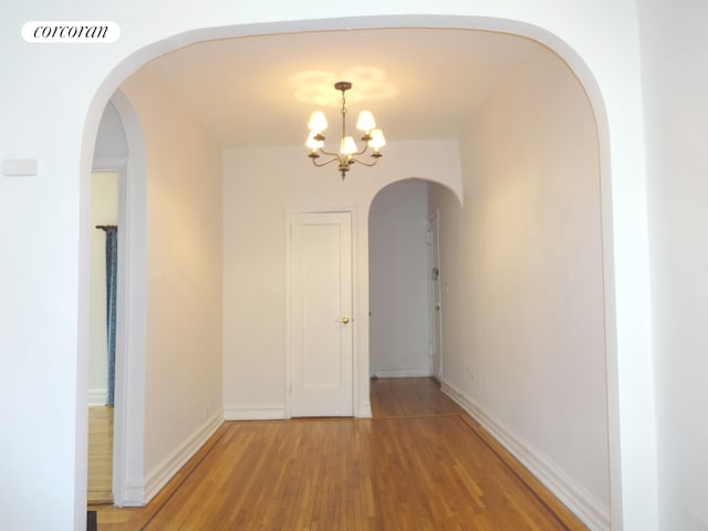 hallway with light wood-style flooring, a chandelier, visible vents, arched walkways, and baseboards