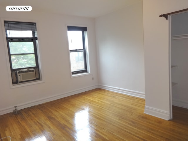 unfurnished bedroom featuring light wood-style flooring, multiple windows, baseboards, and cooling unit