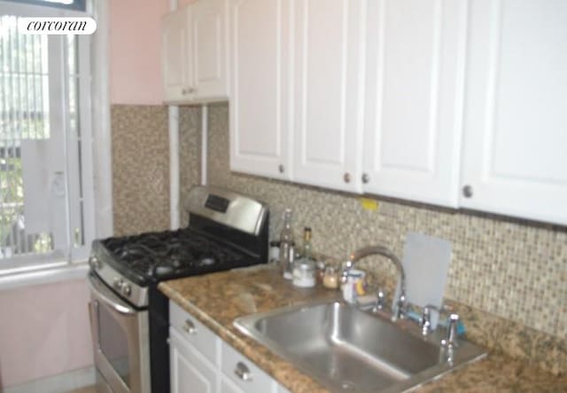 kitchen with stainless steel gas stove, decorative backsplash, white cabinets, and a sink