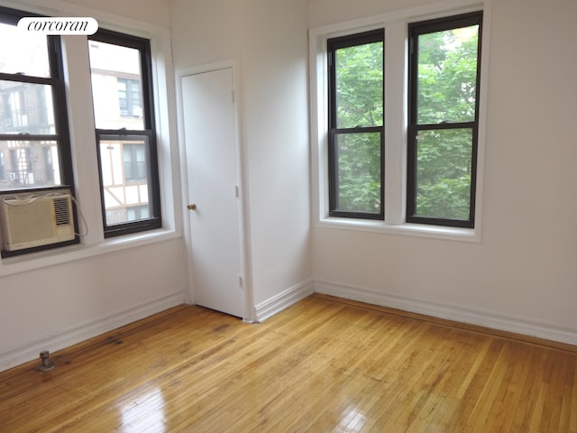 unfurnished room featuring a healthy amount of sunlight, light wood-type flooring, baseboards, and cooling unit