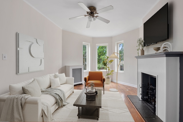 living area with baseboards, a fireplace with raised hearth, ornamental molding, ceiling fan, and wood finished floors